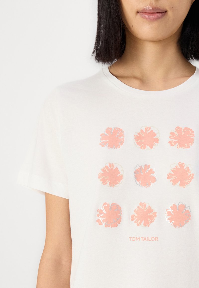T-shirt blanc à manches courtes avec un motif de fleurs roses en grille 3x3 et le texte "TOM TAILOR" en minuscules en dessous. Matériau en coton.