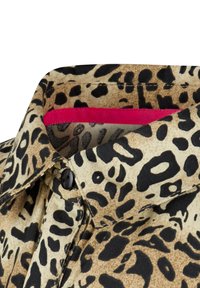 Zoom na límec košile s leopardím vzorem, který obsahuje černé a hnědé vzory, s živým růžovým akcentem uvnitř límce.