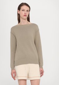 Beige strikkegenser med vid halslinning, ribbede mansjetter og kant. Kombinert med lyse beige shorts med snor og kontrasterende sømmer.