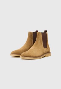 Botas Chelsea de ante en marrón claro con paneles laterales elásticos, punteras redondeadas y una suela de goma en tono beige. Diseño minimalista con detalle de tira.
