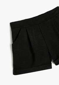 Shorts noirs en tissu texturé, présentant un design plissé et des poches latérales. L'ourlet est roulé pour une finition décontractée.