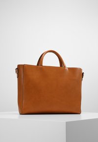 Sac fourre-tout en cuir marron avec des poignées doubles, forme rectangulaire, texture lisse et design minimaliste. Pas de quincaillerie ou d'accents visibles.