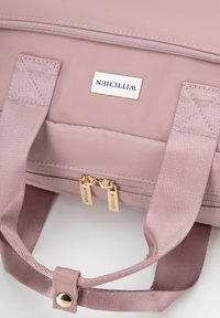 Bolso de nylon rosa con dobles cremalleras doradas, placa de logo, asas de tela resistentes y detalles texturizados. Superficie lisa y diseño minimalista.