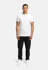 Camiseta blanca de algodón de manga corta combinada con pantalones cargo negros, que cuenta con múltiples bolsillos y un cordón. Se lleva con zapatillas blancas.