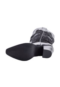 Botas de vaquero negras con punta afilada y tacón bajo apilado, mostrando la suela y la costura decorativa en la parte superior.