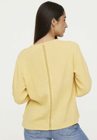 Haut à manches longues jaune en tissu froissé. Présente une accent en dentelle au milieu du dos. Encolure arrondie, coupe décontractée et texture douce.