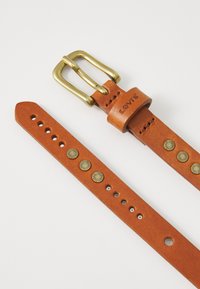 Ceinture en cuir marron avec une boucle en laiton, ornée de clous en métal décoratifs et de plusieurs trous pour l'ajustement. Nom de la marque embossé sur la sangle.