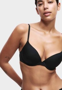 Sujetador negro acolchado con tirantes ajustables, presenta una textura suave y escote pronunciado, diseñado para levantar y ofrecer soporte.