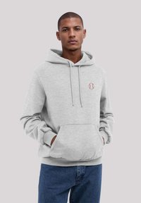 Grauer Kapuzenpullover mit einer Vorderstasche, verstellbarem Kordelzug und einem kleinen gestickten Baseball-Logo. Kombiniert mit dunklen Jeans.