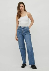 Jeans azules de tiro alto con corte recto, confeccionados en denim de textura suave. Combinados con una camiseta ajustada blanca.