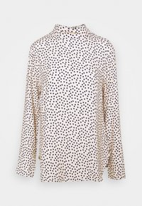 Maglietta a maniche lunghe color crema con pois neri irregolari e colletto alto, esposta su uno sfondo bianco.