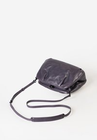 Lila Leder Umhängetasche mit weicher Textur, Klappenverschluss, verstellbarem Riemen und dezentem Branding auf der Vorderseite.