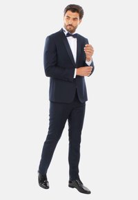 Abito navy con finitura in satin, camicia bianca e papillon nero. Design slim fit con pantaloni su misura e scarpe lucide nere.