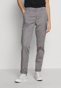 Lichtgrijze katoenen broek in een slim fit, met zijzakken en opgerolde zoom, gecombineerd met witte sneakers.