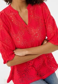 Blusa rossa in pizzo con motivi floreali, scollatura a V e maniche corte a palloncino, realizzata in tessuto testurizzato e con bordi smerlati.