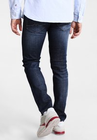 Slim-fit mörkblå denimjeans med en subtil textur, med bågformade bakfickor och en ren fåll, som matchas med vita sneakers.
