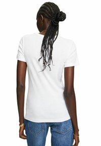 T-shirt bianco in cotone con maniche corte, scollo a costine e silhouette aderente, abbinato a jeans blu. Texture liscia, design semplice.