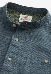 Camicia blu navy con bottoni, caratterizzata da un motivo a quadretti testurizzato, colletto alla coreana, due bottoni e tessuto interno a contrasto con motivo.