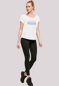 Balta trumpa rankovėmis marškinėliai su "JASMINE" grafika purpurine ir žalia spalvomis, derinami su juodomis kelnių leggings ir juodais sportiniais bateliais.