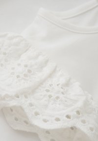 Witte top met gestructureerde kantdetails met bloemmotieven langs de zoom, van een gladde katoenstof en een eenvoudige ronde halslijn.