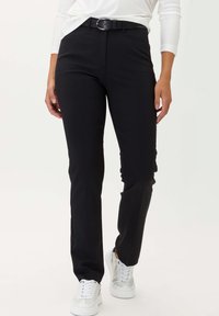 Pantaloni neri su misura con vestibilità slim, dotati di tasche laterali e una cintura nera texturizzata con fibbia argentata. Abbinati a sneakers bianche.