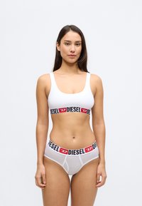 Λευκό αθλητικό σουτιέν από βαμβάκι με μαύρη και κόκκινη ταινία λογότυπου "DIESEL", συνδυασμένο με αντίστοιχα ανοιχτό γκρι εσώρουχα που έχουν το ίδιο σχέδιο ταινίας.