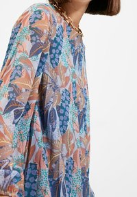Bluse mit Blumenmuster in Blau-, Pink- und Orangetönen, hergestellt aus leichtem Stoff mit rundem Ausschnitt und langen, plissierten Ärmeln.