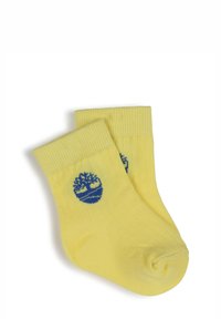 Chaussettes en coton jaunes avec des bords côtelés, arborant un logo d'arbre bleu sur le côté. Le design est simple et ajusté.