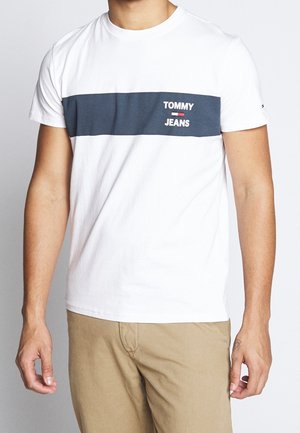 White cotton t-shirt featuring a navy horizontal stripe and "TOMMY JEANS" printed in white. Short sleeves, crew neck design, and relaxed fit.