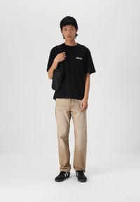 Sort bomuld t-shirt med grafisk print, beige denim bukser og sorte sneakers med hvide striber. Lille sort skuldertaske.