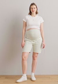Hvit kortermet skjorte og grønne stripete graviditetsshorts. Shortsene har elastisk midjebånd for komfort. Brukt med hvite sneakers.