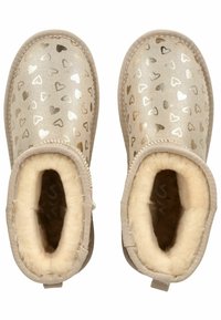 Beige Stiefeletten mit metallischen Herzmustern, weichem Futter aus Fell und rohen Kanten. Rundes Zehendesign und genähte Akzente.