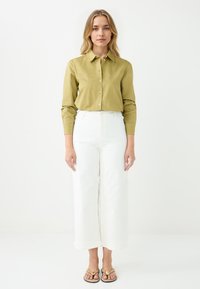 Olive green button-down shirt with long sleeves, paired with white wide-leg pants and brown sandals with a decorative buckle.
