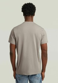 Camiseta gris de manga corta hecha de algodón, con cuello redondo y un corte relajado. Diseño simple con textura suave, vista desde la parte de atrás.