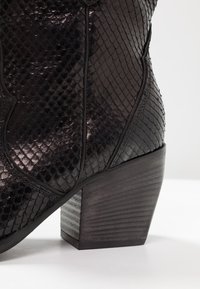 Bottine en cuir noir avec un motif reptilien texturé, dotée d'un talon en bois empilé et de détails de couture subtils.