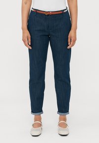 Pantalon en denim bleu marine avec une coupe droite et un ourlet retroussé, accompagné d'une ceinture marron avec une boucle ronde. Porté avec des chaussures claires.