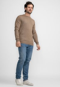 Lichtbruine ronde hals trui, slim fit ontwerp, gedragen met blauwe jeans en witte sneakers. Glad oppervlak, geen zichtbare patronen of logo's.