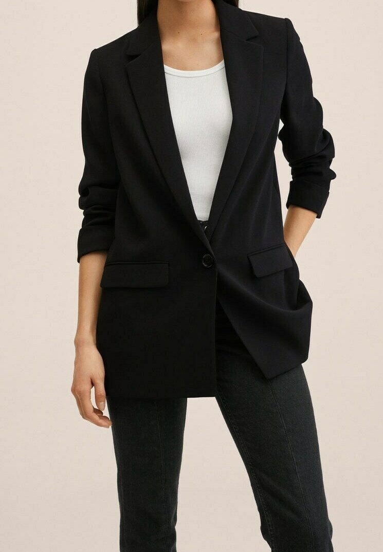 Blazer noir avec un col cranté, une fermeture à un bouton et deux poches avant. Porté sur un débardeur blanc, manches retroussées.