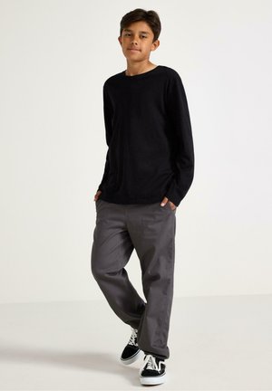 Zwarte lange mouwen T-shirt gecombineerd met grijze broek en zwart-witte sneakers. De broek heeft een rechte snit en details van zakken.