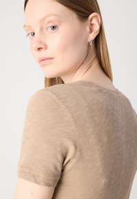Beige lyhythihainen paita pyöreällä kaula-aukolla, jossa on pehmeä, hieman teksturoitu kangas ja siistit ompeluyksityiskohdat saumoissa.