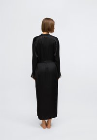 Čierny saténový župan s dlhými rukávmi a čipkovými manžetami. Obsahuje viazací opasok a jemný detail na chrbte. Hladká textúra s plným, plynulým strihom.