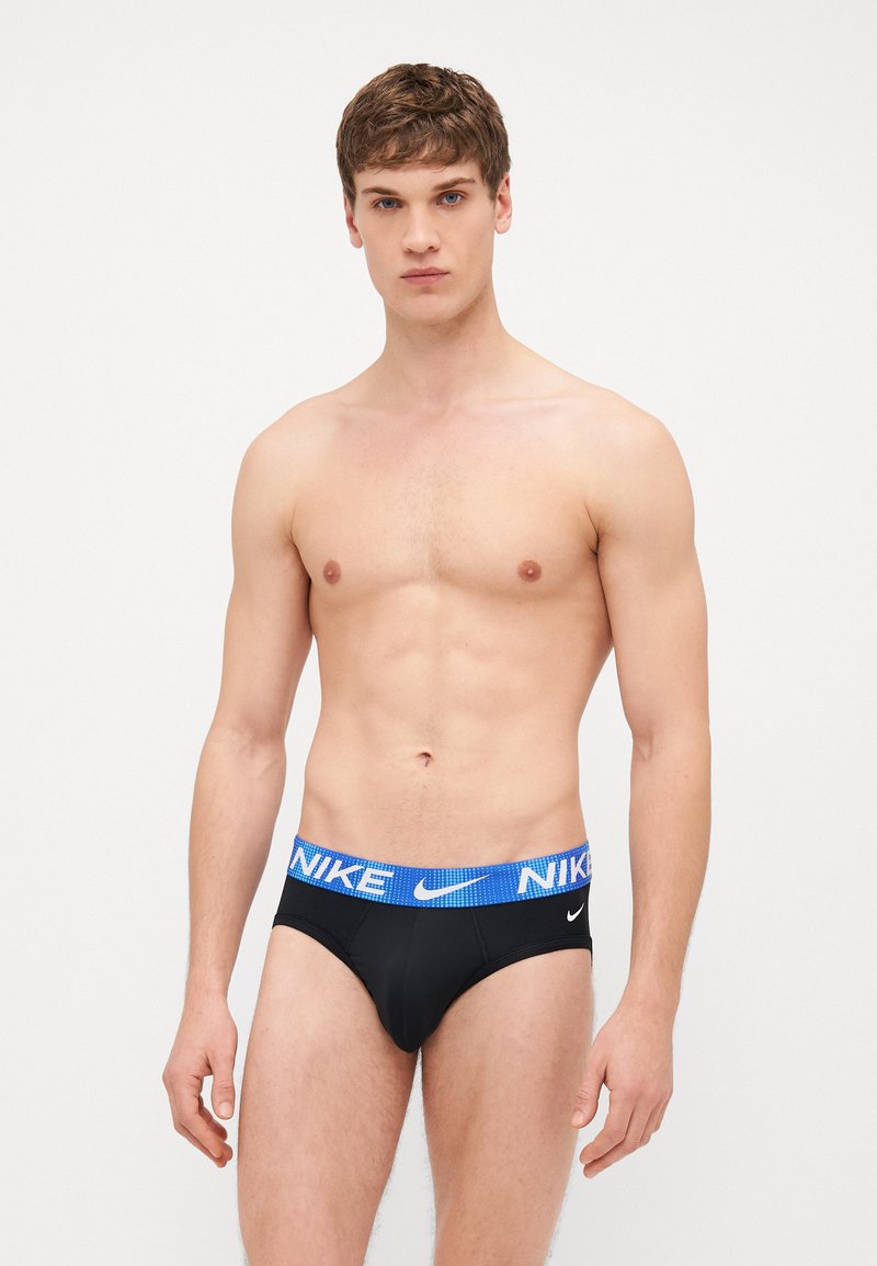 Un slip de bain noir avec une ceinture à logo Nike bleu. Le tissu est doux et le design présente une coupe ajustée avec une couverture minimale.