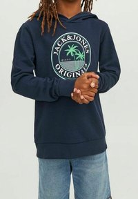 Marinblå hoodie med dragsko i huvan, vit cirkulär logotyp med palmträd och text, ribbade ärmslut och nederkant, kombinerad med ljusblå shorts.