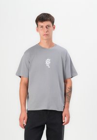 Grå bomulds T-shirt med korte ærmer, prydet med et hvidt dragegrafik på brystet. Lige snit, blød tekstur og rund halsudskæring.