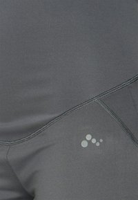 Leggings atléticos cinzentos, com um tecido suave e elástico, apresentando um design de costura visível e um pequeno logótipo no canto inferior.