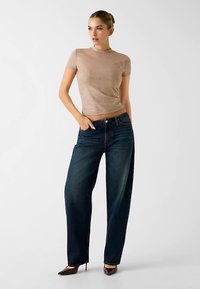 Beige kortärmig top met structuur, gecombineerd met losse, donkerblauwe spijkerbroeken en bruine pumps met een puntige neus. Eenvoudig, aansluitend design zonder zichtbare patronen.