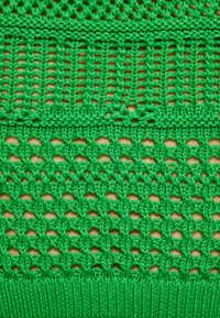 Țesătură tricotată verde, cu un design deschis, având secțiuni alternative de solid și plasă, texturată cu un bordaj cu nervuri la baza.