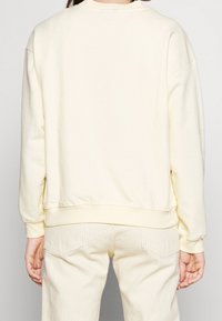 Bluza w kolorze kremowym z opuszczonymi ramionami, ściągaczami na rękawach i u dołu. Miękka w dotyku, o prostym wzornictwie, bez widocznych logo czy wzorów.