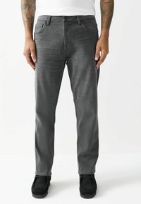 Grå denim jeans med slim fit, fem-lommer design og knaplukning. Bæret med sorte ruskind sko, der viser en glat tekstur.