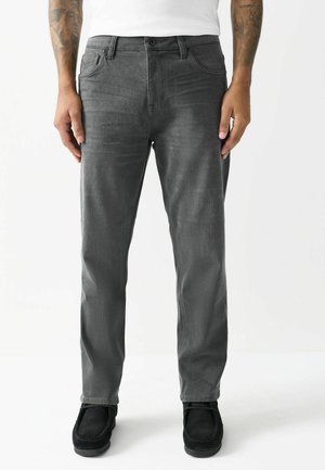 Graue Denim-Jeans mit schlankem Schnitt, Fünf-Taschen-Design und Knopfverschluss. Getragen mit schwarzen Wildlederschuhen, die eine glatte Textur zeigen.